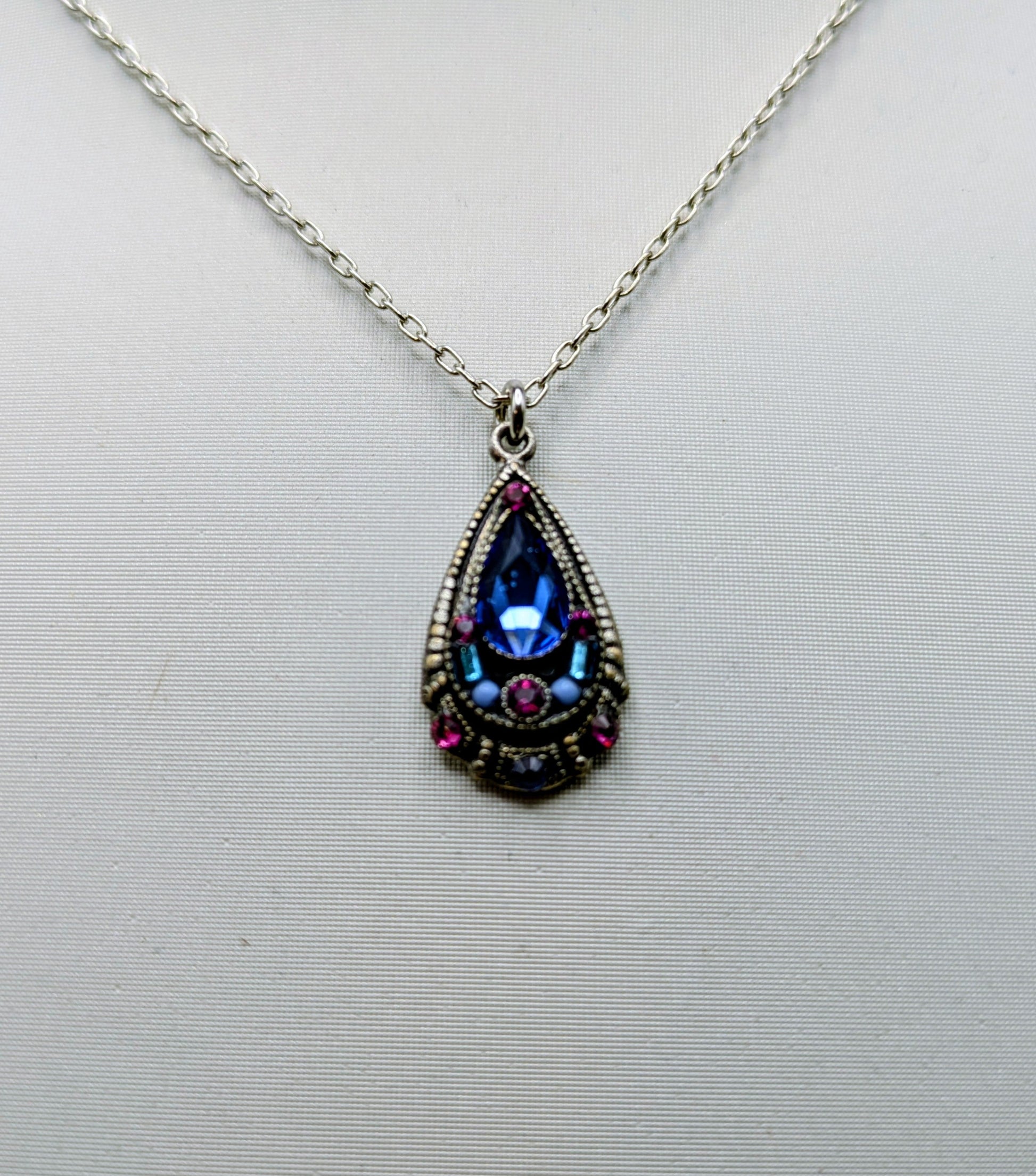 Teardrop-shaped pendant with colorful gemstones on a white background