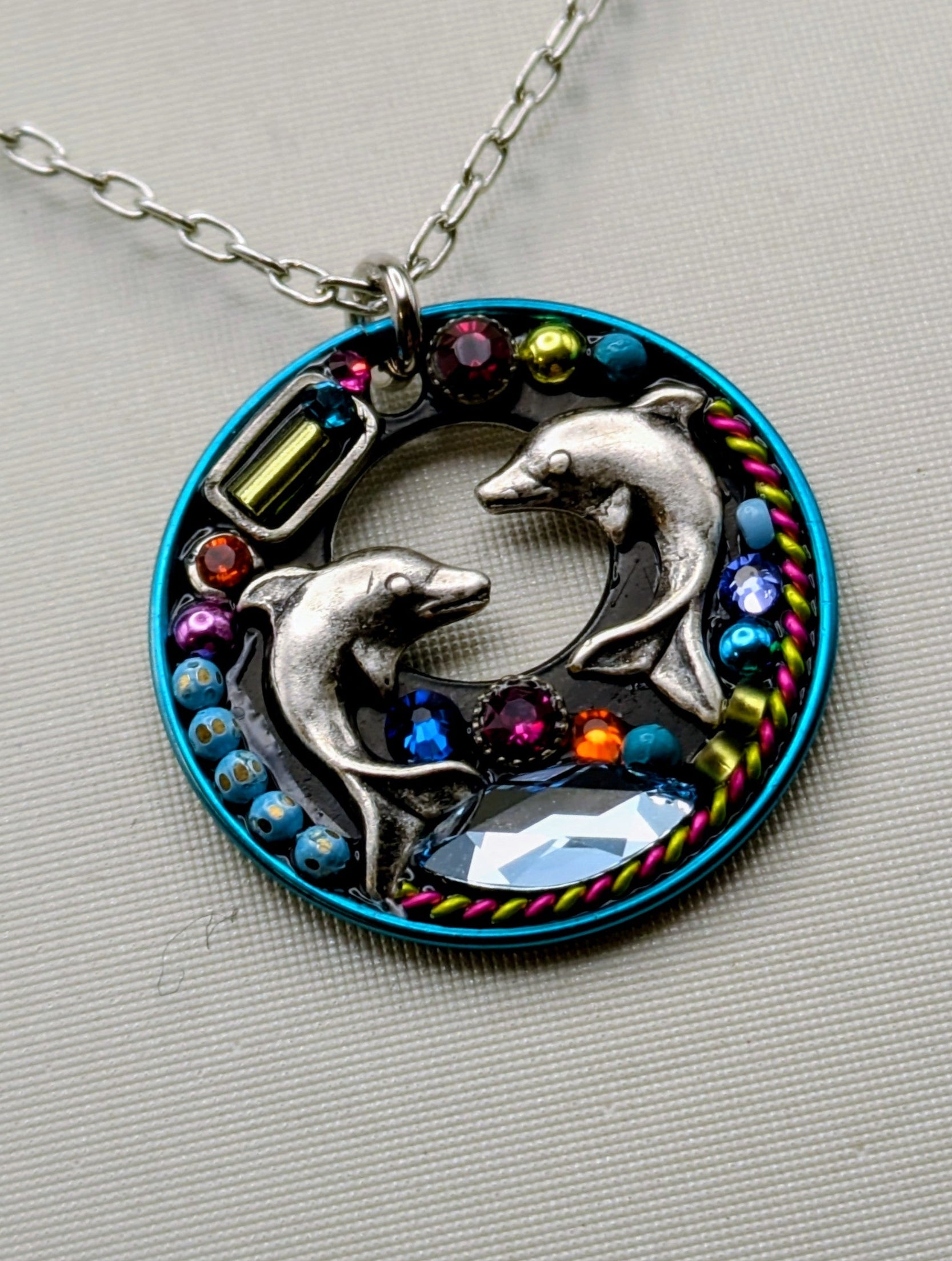 Necklace with a circular pendant featuring two dolphins and colorful stones on a gray background