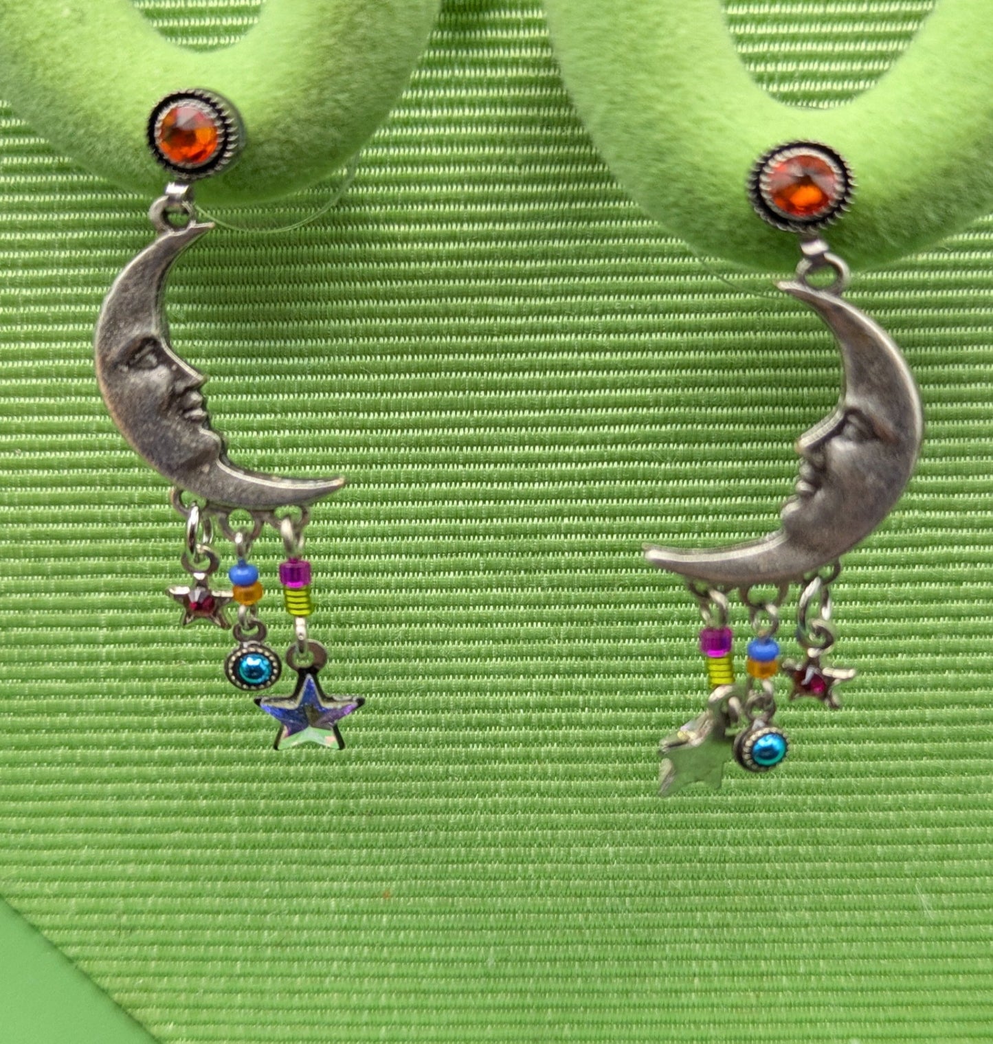 Pair of earrings with colorful charms on a green earring stand.