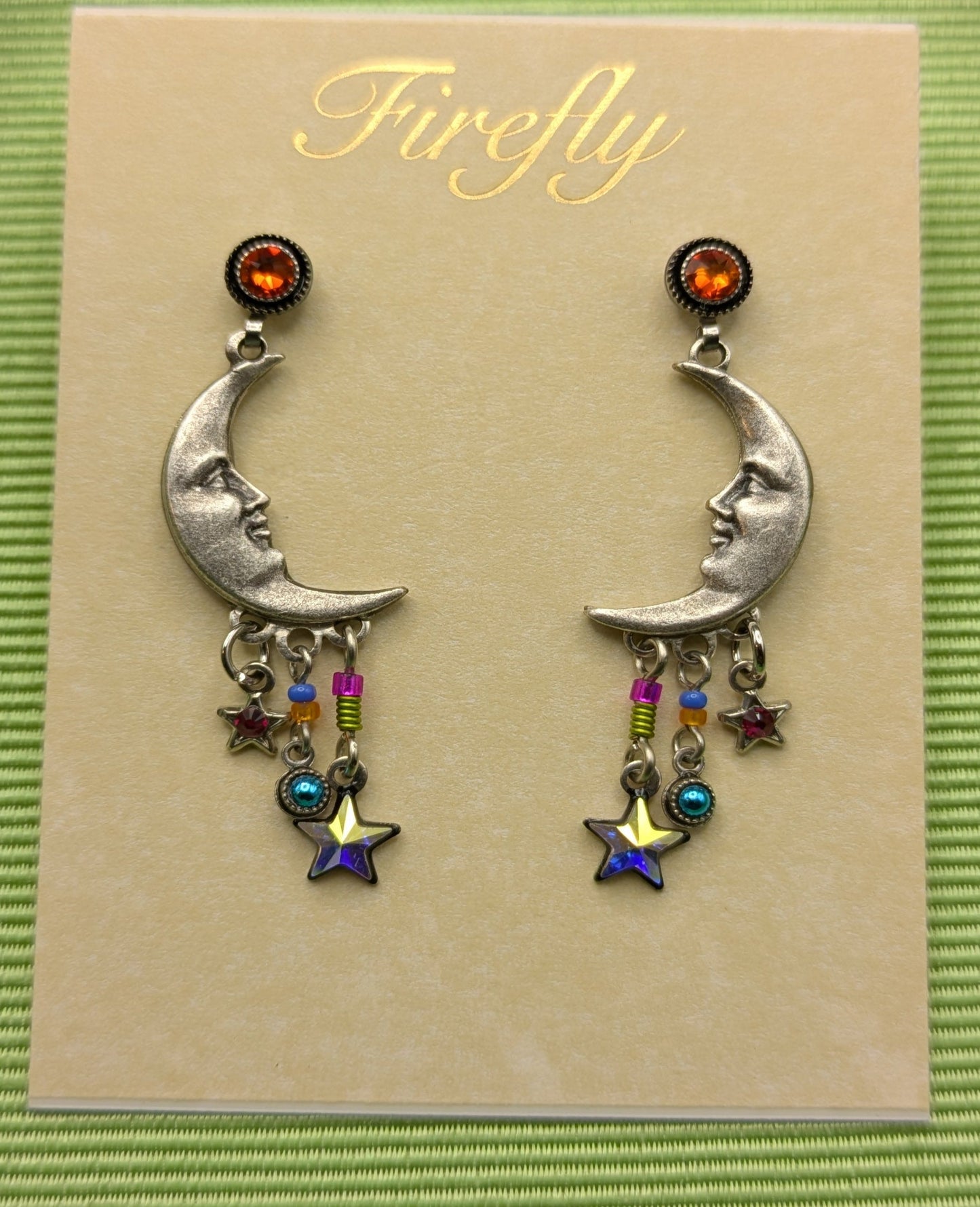 Pair of silver earrings with colorful charms on a 'Firefly' branded card, set against a green background.