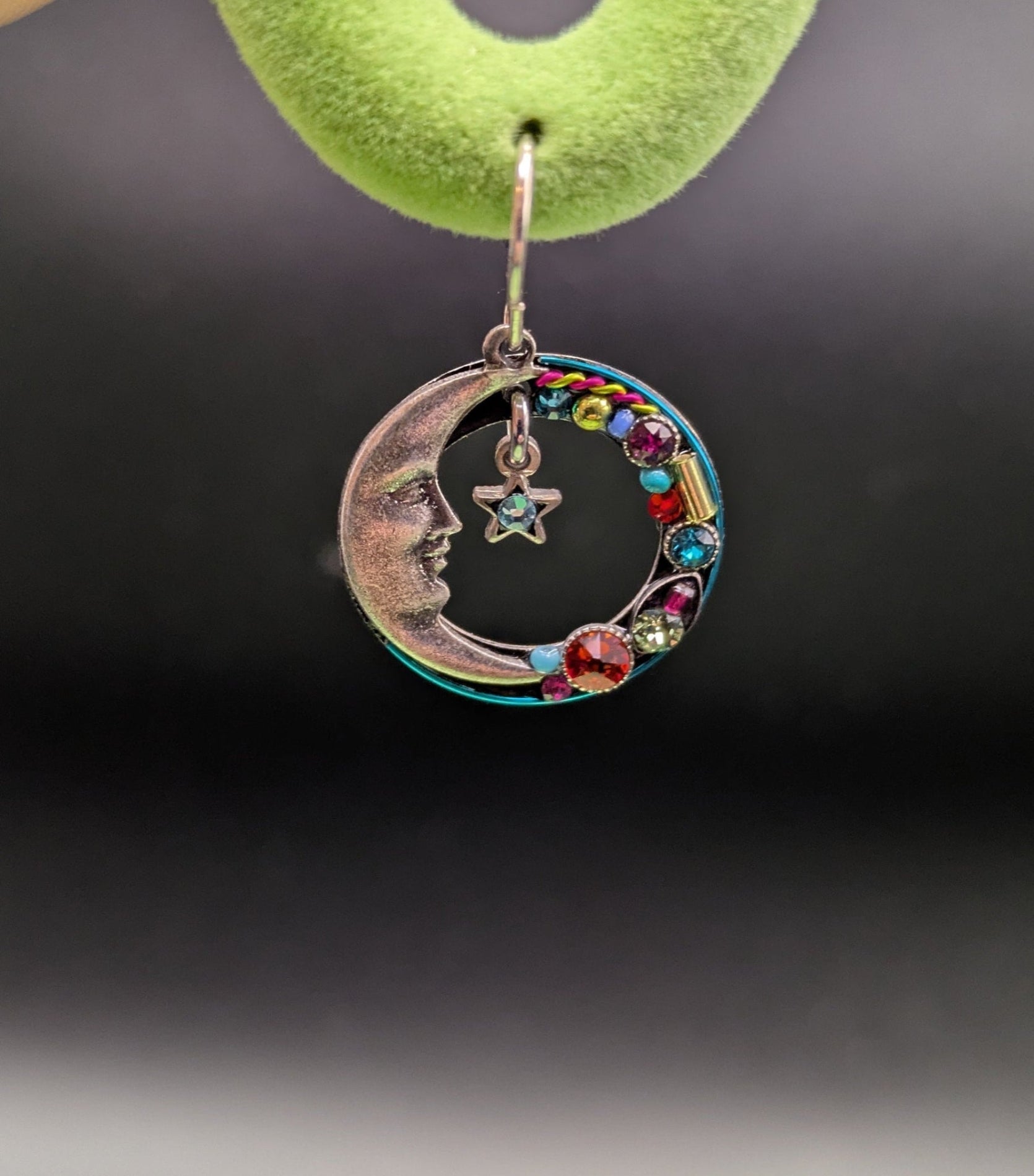 Earring with colorful beads hanging from a green hook against a dark background