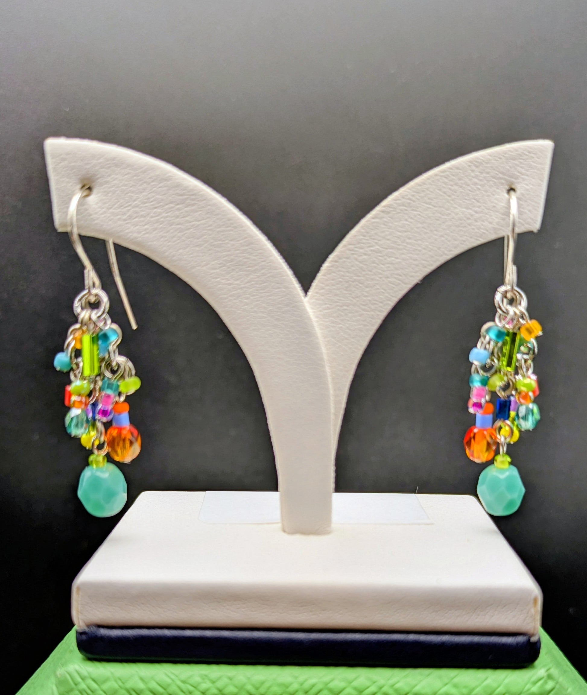 Colorful beaded earrings on a white earring stand against a black background