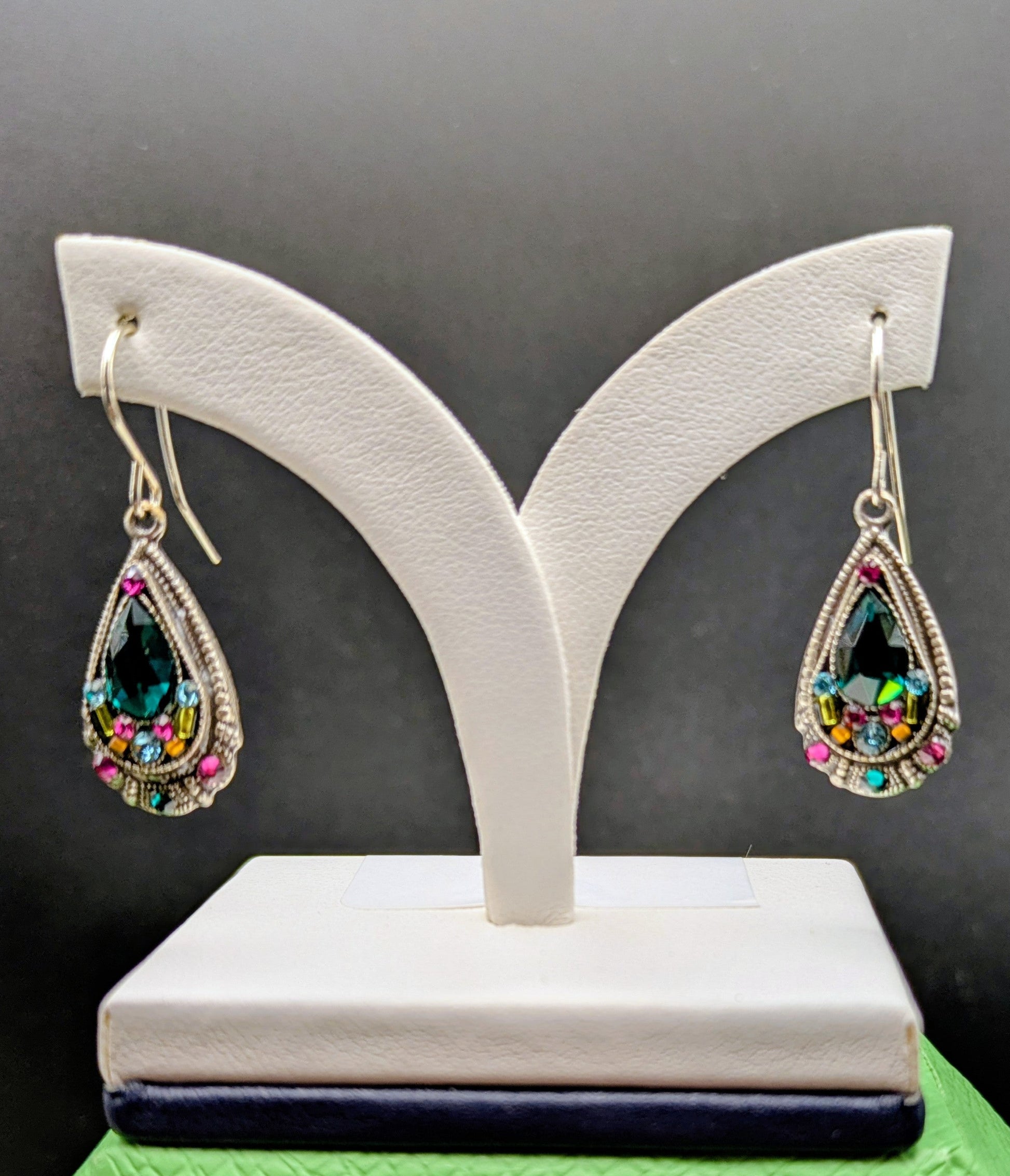 Teardrop-shaped earrings with colorful gemstones on a white stand against a black background.