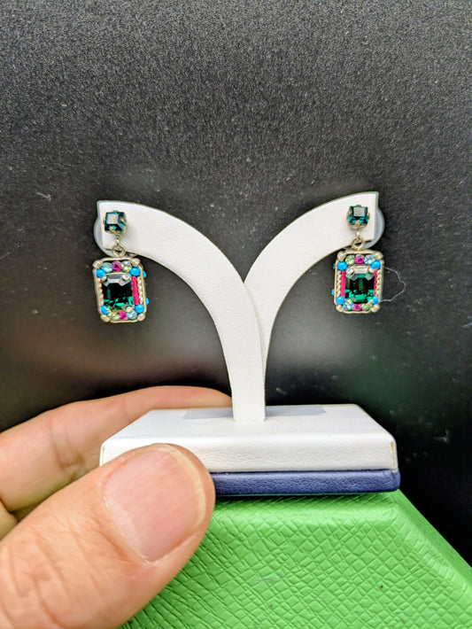 Colorful earrings on a white stand held by a hand against a dark background