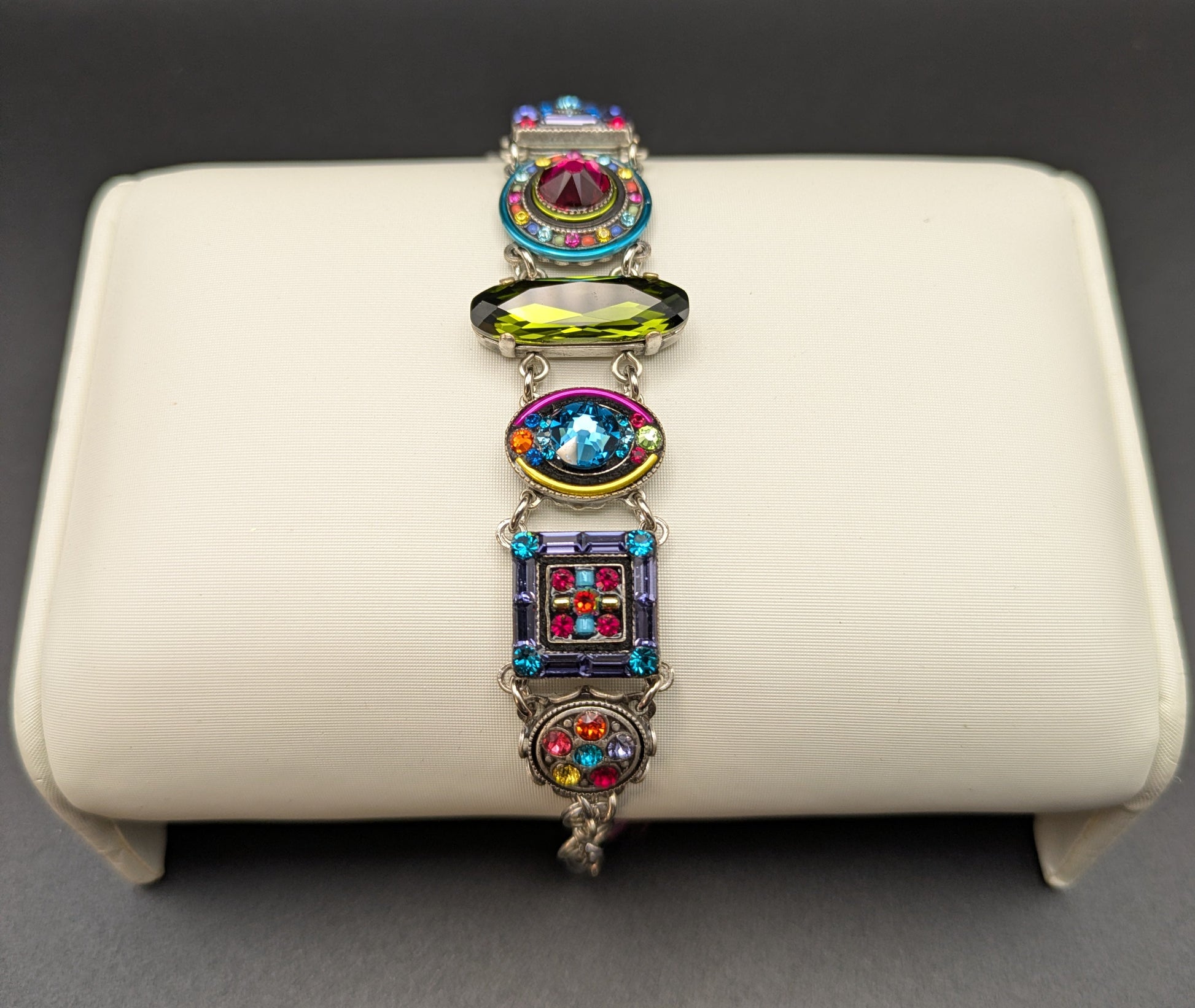Multicolored gemstone bracelet on a white cushion against a dark background