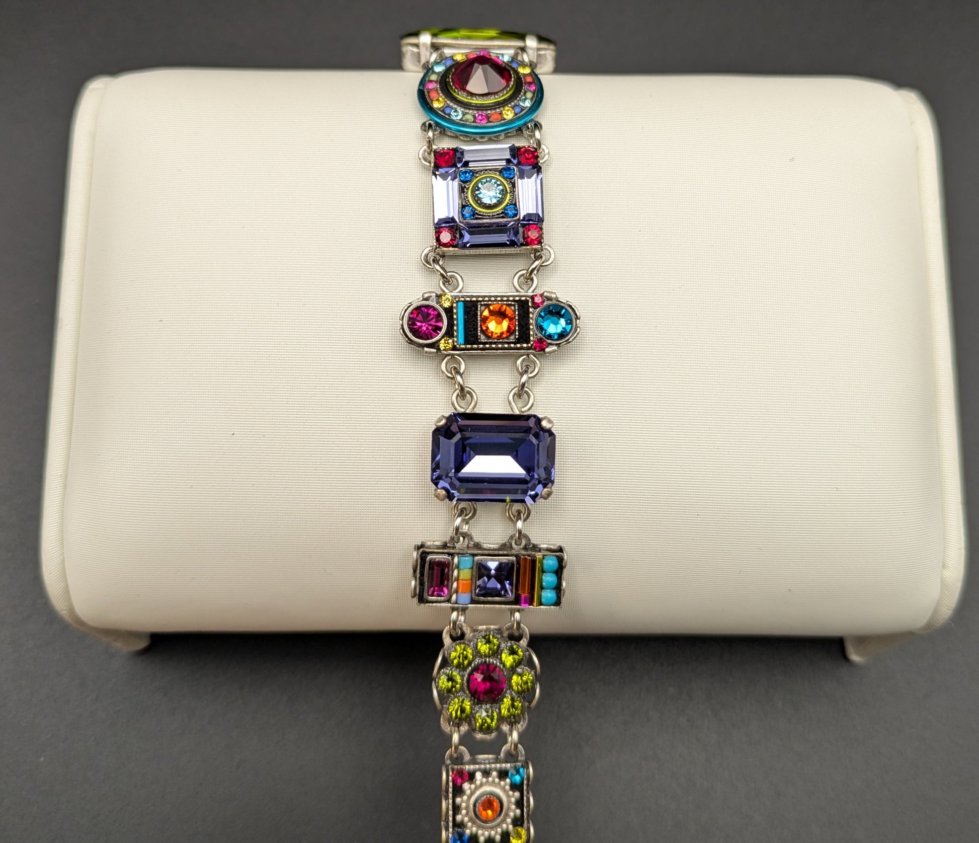 Multicolored gemstone bracelet on a white jewelry display box against a dark background
