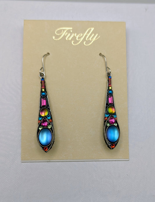 A pair of ornate drop earrings displayed on a beige card labeled 'Firefly.' The earrings have silver-toned hooks and dark metal settings with multiple colorful stones, including blue oval centers, pink and yellow accents, and small red details.