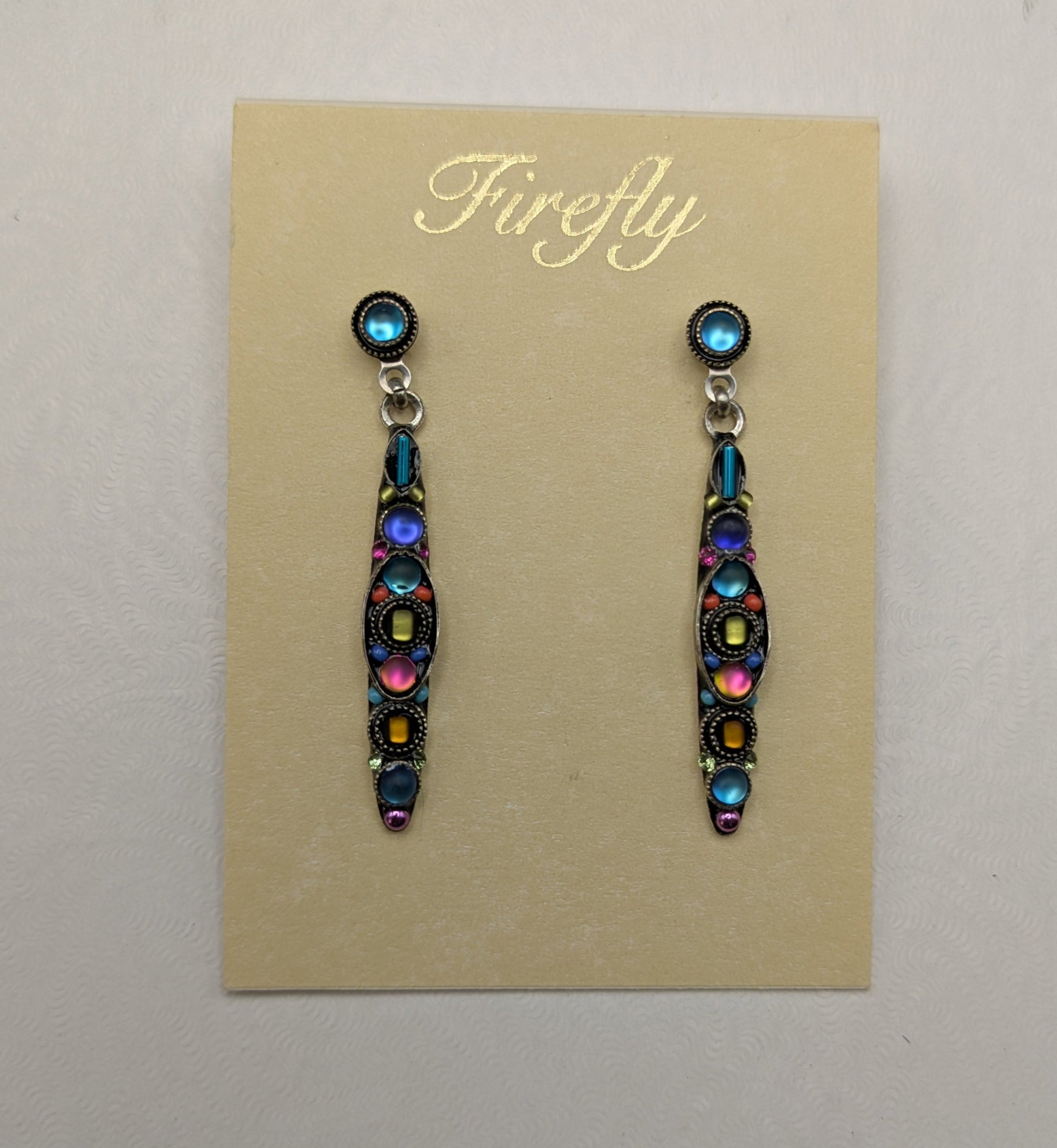 A pair of Firefly brand dangle earrings displayed on a beige card insert, set against a white gift box on a neutral gray background.
