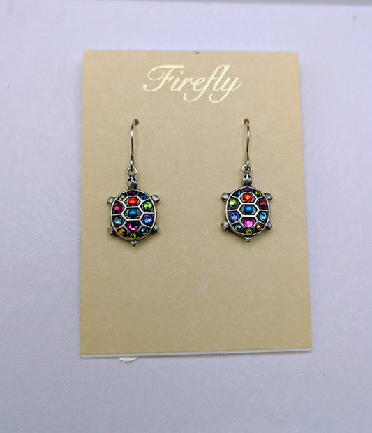 A pair of Firefly brand dangle earrings with colorful faceted crystal-like centers and silver-toned hooks, displayed on a beige card over a white box.