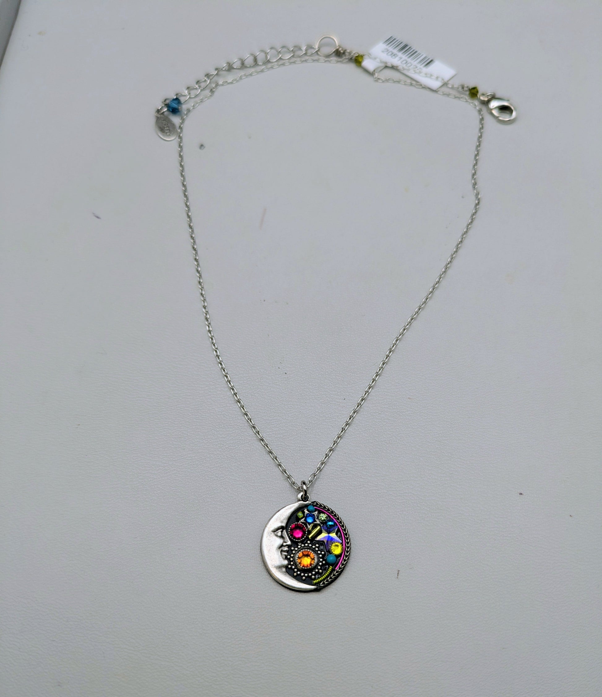 A silver chain necklace with a round silver pendant featuring a colorful, hand-painted hamsa design, displayed on a light gray surface.