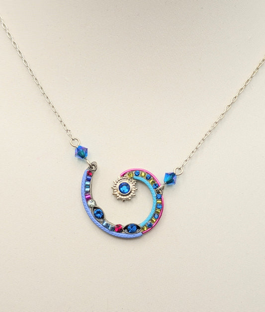 A silver chain necklace with a colorful spiral pendant on a white display bust. The spiral pendant features blue, pink, and orange details, with a central blue gemstone.