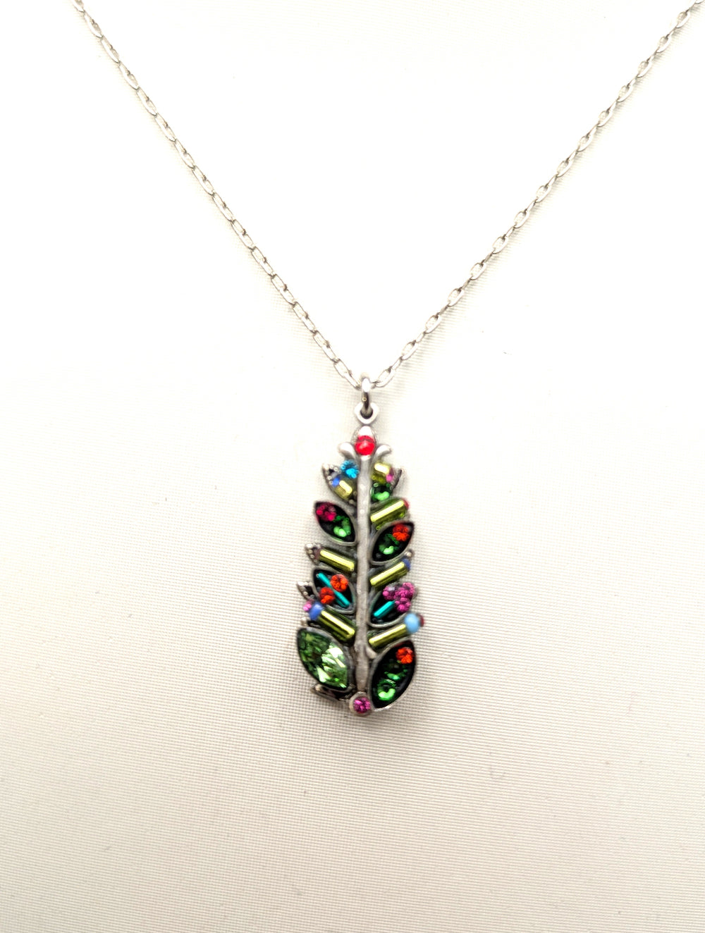 A silver chain necklace with a leaf-shaped pendant adorned with colorful rhinestones in green, red, pink, and blue, displayed against a plain white background.