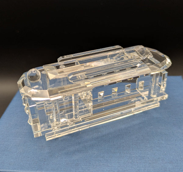 Clear crystal model of a tram on a blue surface with a dark background