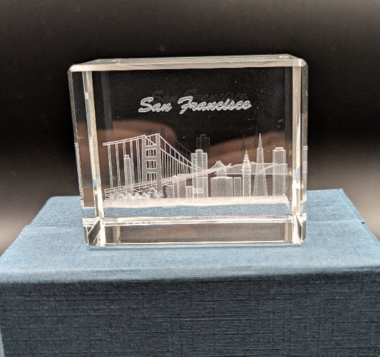 Crystal model of a cityscape with 'San Francisco' engraved on it, placed on a blue cushion.