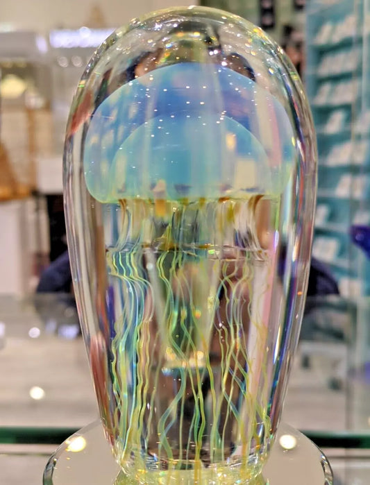 Satava Art glass sculpture of a jellyfish with a clear dome shape, featuring a blue and gold band with colorful, wispy tentacles inside.