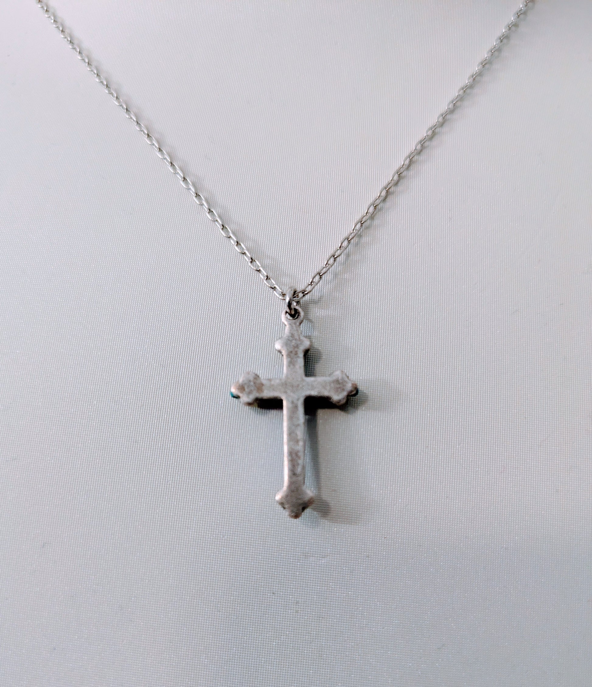 Silver tone cross pendant on a chain against a light gray background