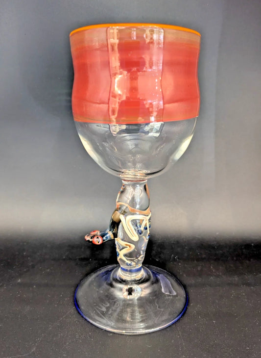 Glass goblet with a red top and frog on stem on a dark surface