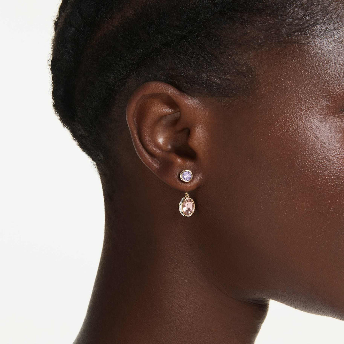A model is wearing gold tone earrings with pink and purple gemstones on a white background.