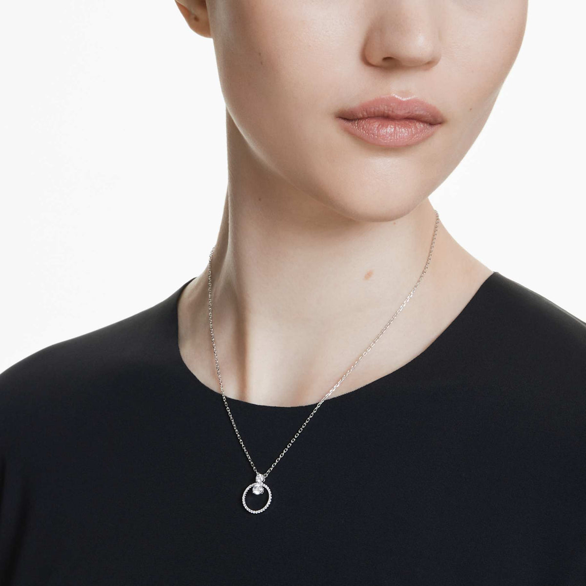 Model is wearing a rhodium-plated silver pendant with a round cut white crystal, attached to a silver chain.