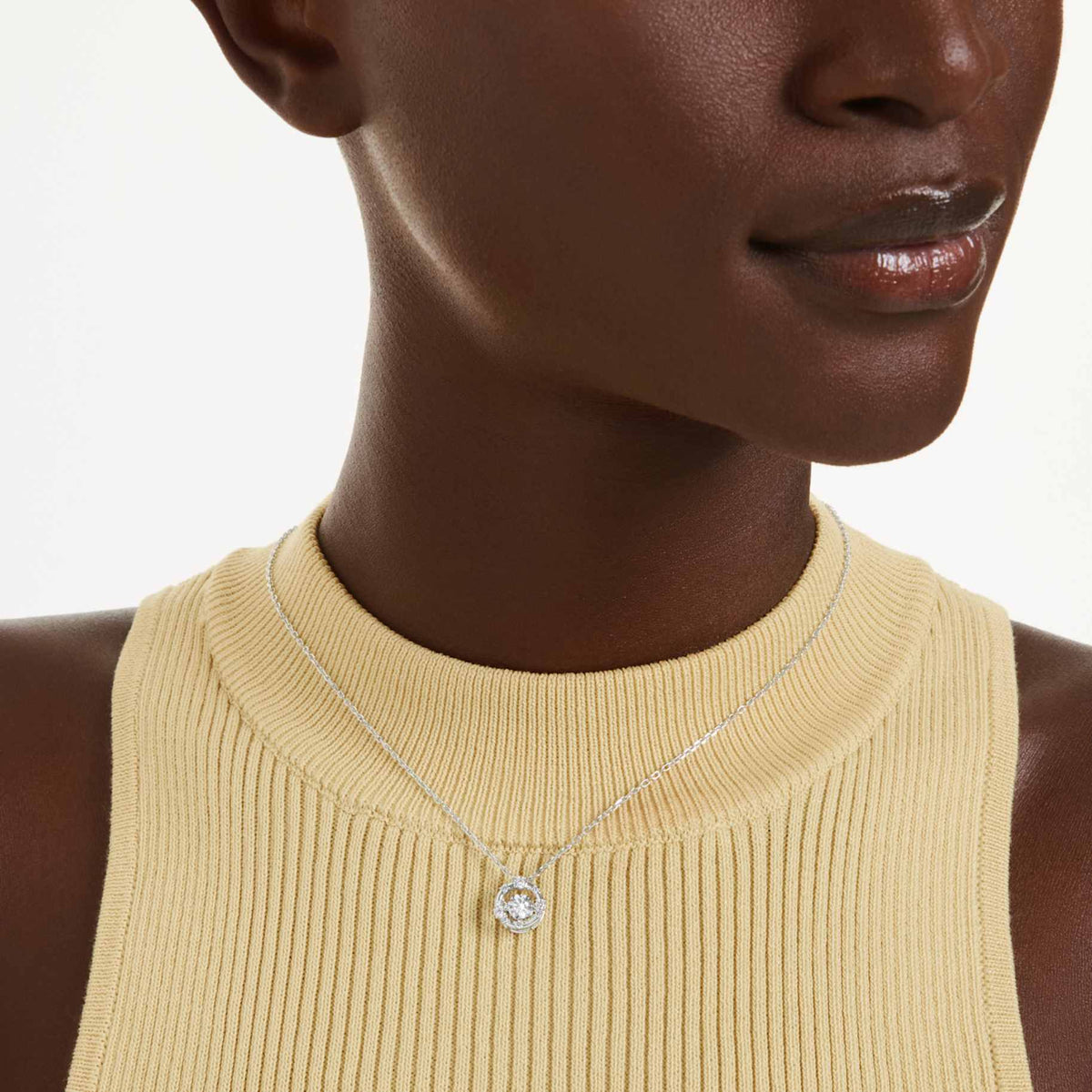 Model wearing the Swarovski Constella clear crystal pendant necklace over a pale yellow ribbed top.