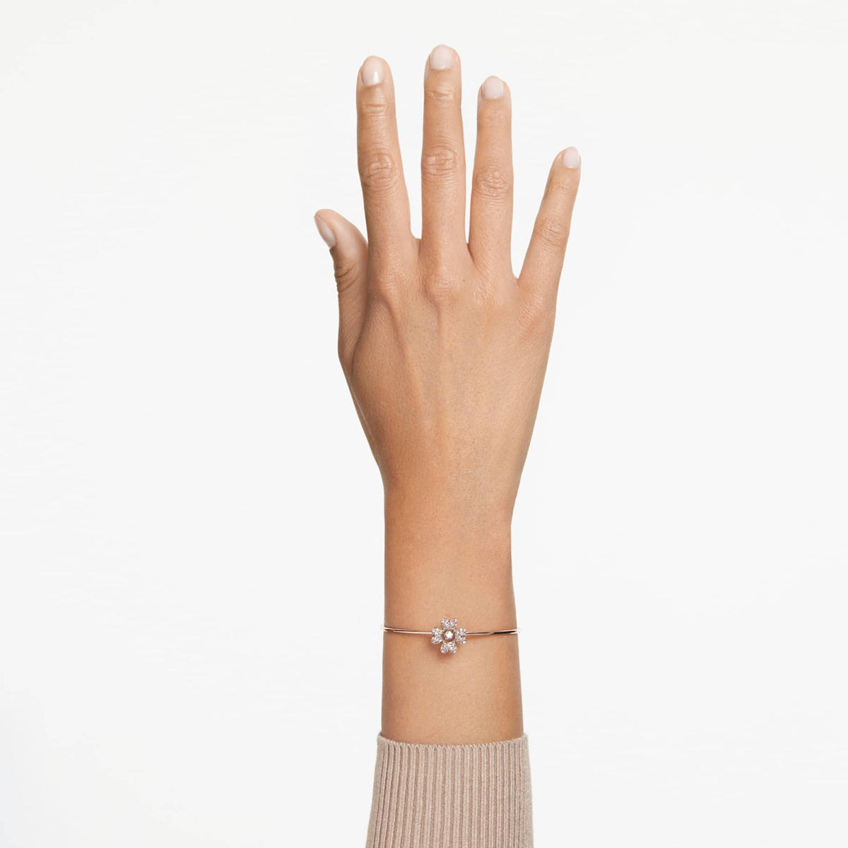 A rose gold-tone plated bracelet with a clover-shaped charm adorned with white crystals in the center on wrist.