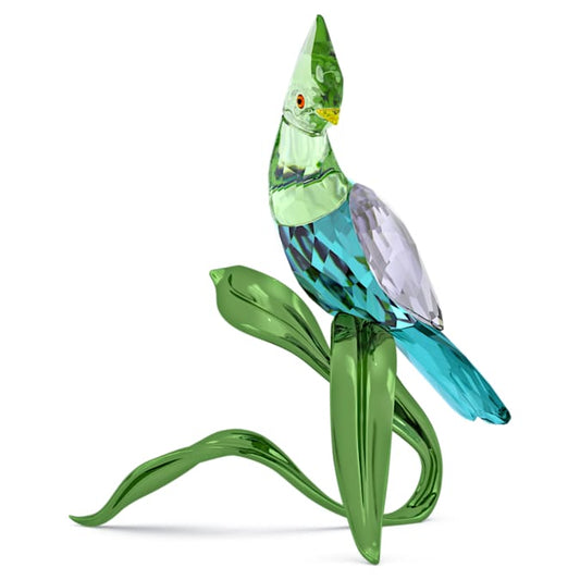 A Swarovski crystal figurine of a green turaco with blue and red details, standing on a green base that resembles a plant.