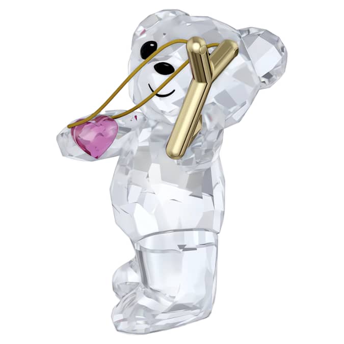 A crystal figurine of a smiling bear with a pink heart and a gold-tone metal slingshot on white background.