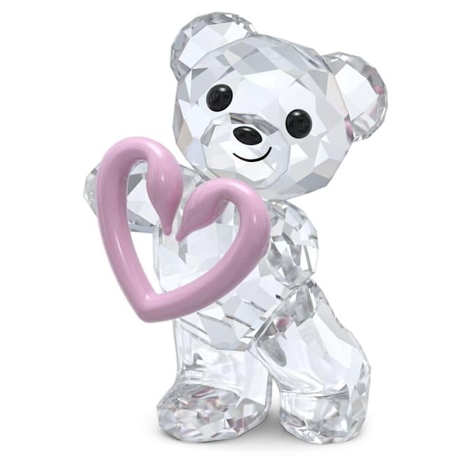 A crystal figurine of a teddy bear holding a pink heart-shaped motif, with a radiant heart shape formed by two Swarovski swans in the background.
