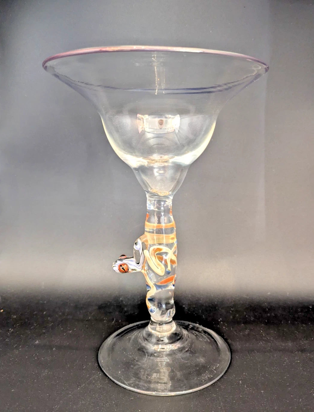 Clear glass martini glass with a decorative stem on a dark surface.