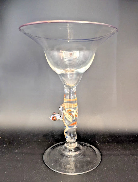Clear glass martini glass with a decorative stem on a dark surface.