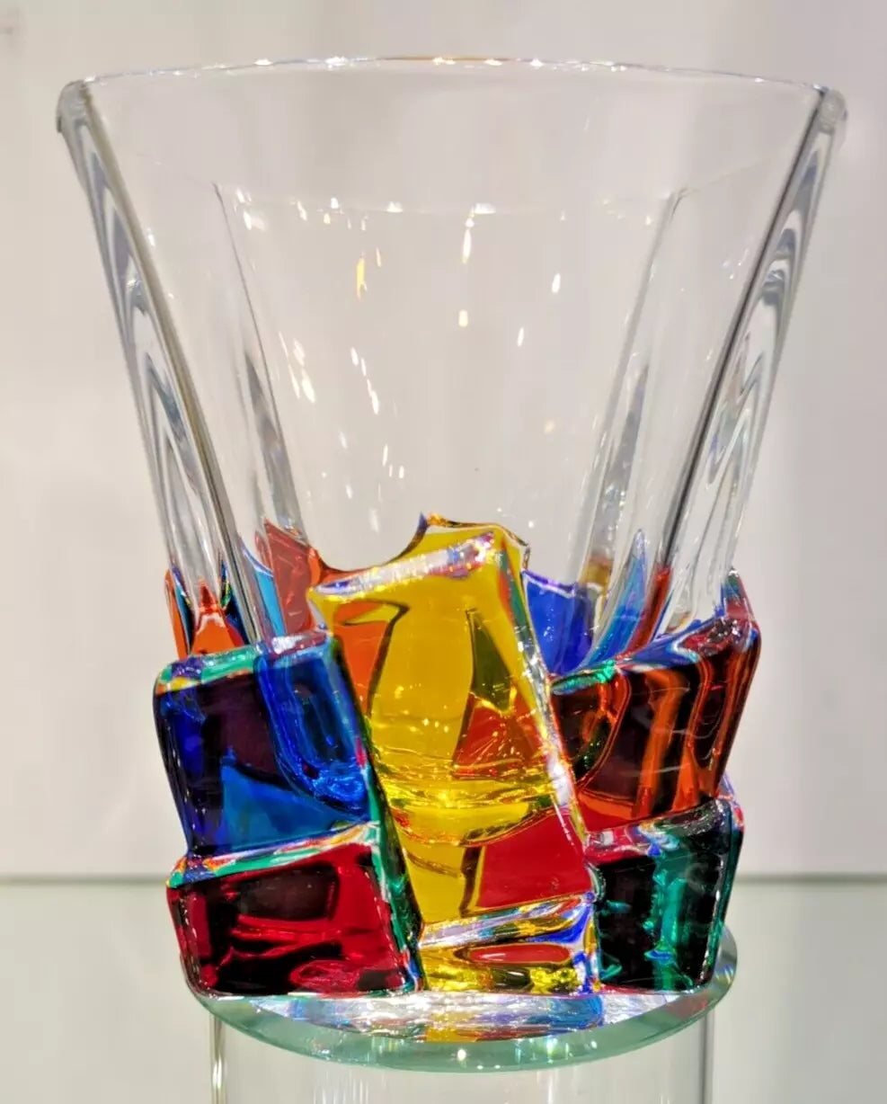 A clear glass whiskey tumbler with multicolored pieces embedded within it.