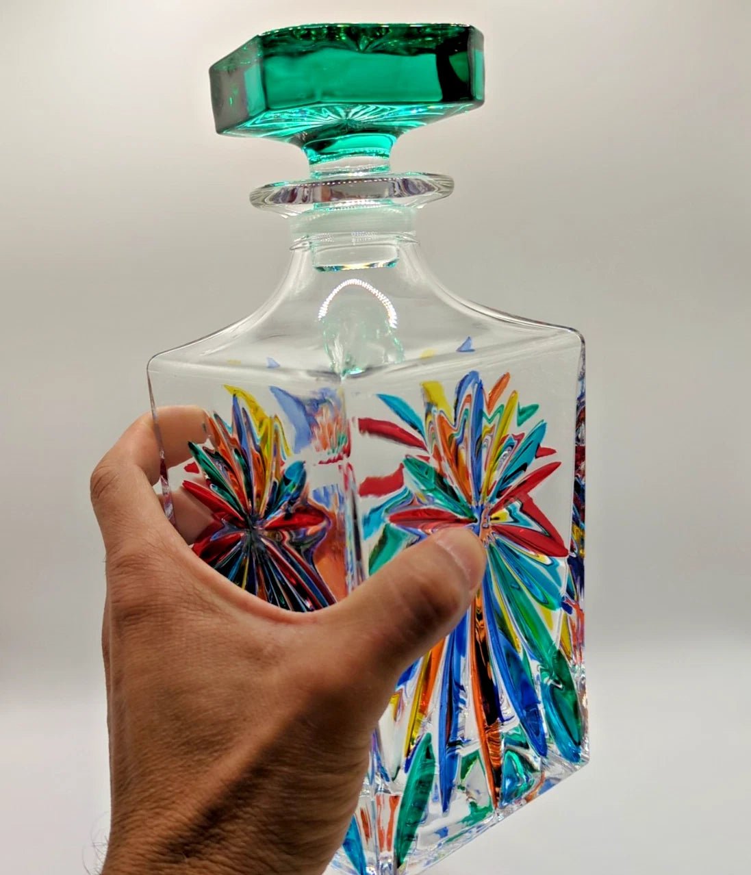Multi color decanter with green lid held by hand.