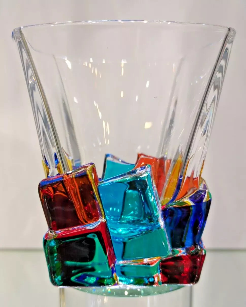 A clear glass whiskey tumbler with multicolored pieces embedded within it.
