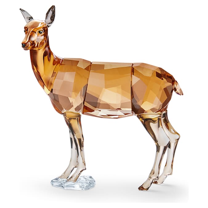 A Swarovski crystal figurine of a doe standing on a clear base, with a mix of amber and clear crystal detailing.