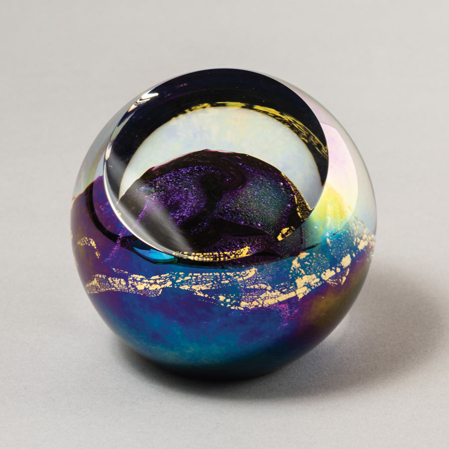 A multicolored glass paperweight with swirling patterns of magenta, violet, pink, and gold, presented on a neutral background.