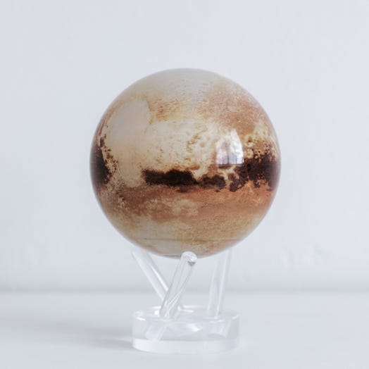 A 4.5 inch diameter globe representing Pluto, with color shading and geographical features, placed on a clear stand.
