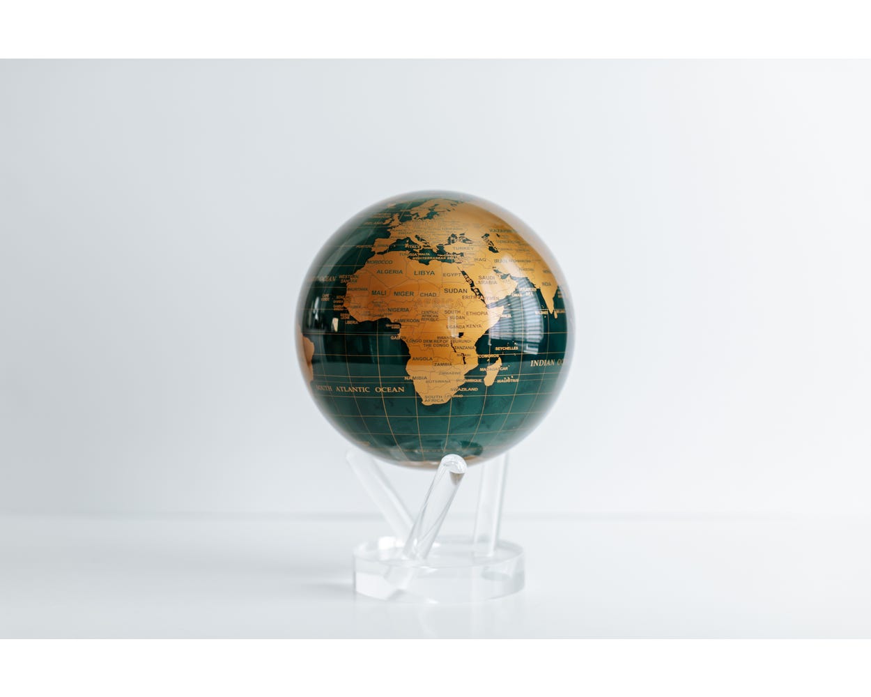 A 6 inch diameter globe with green and gold coloring, displayed on a clear stand, featuring smooth, flowing lines to represent country boundaries.