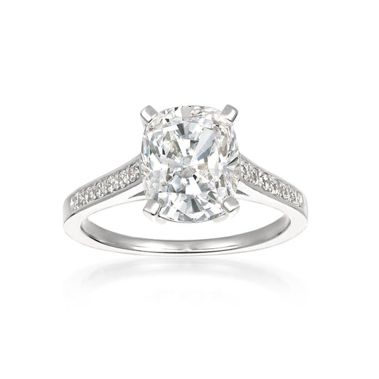 A cushion cut diamond ring with smaller stones set in a band, finished in platinum.