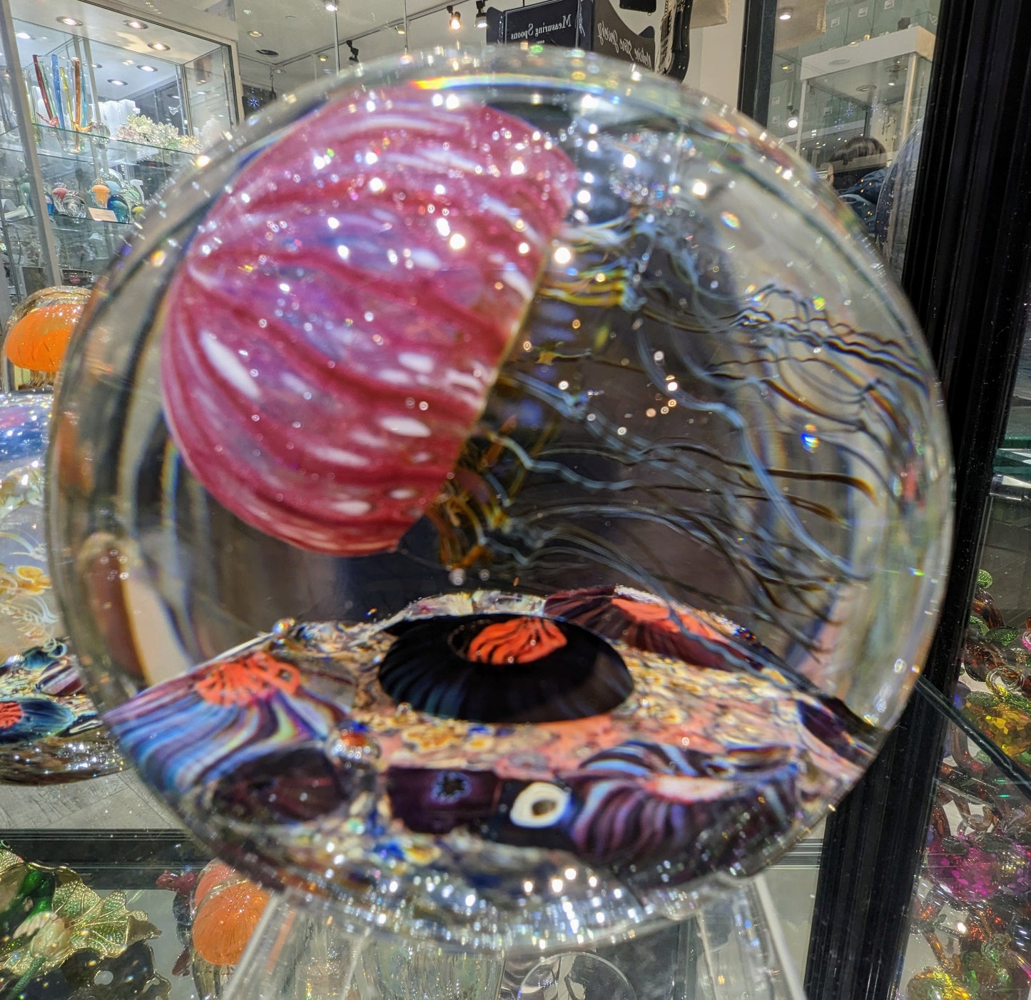 A handcrafted Satava art glass jellyfish sculpture with a gold and ruby colored body, side view