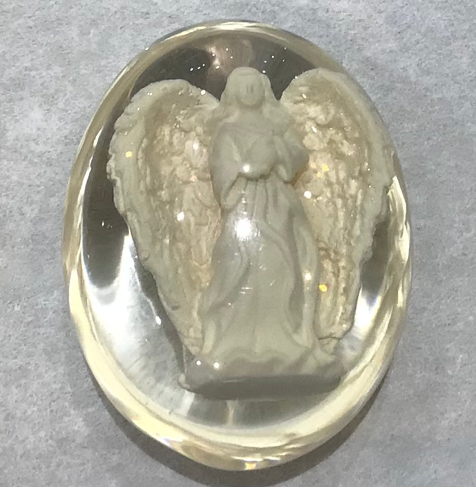 A resin stone craft of an angel standing with wings spread, enclosed in a clear oval casing.