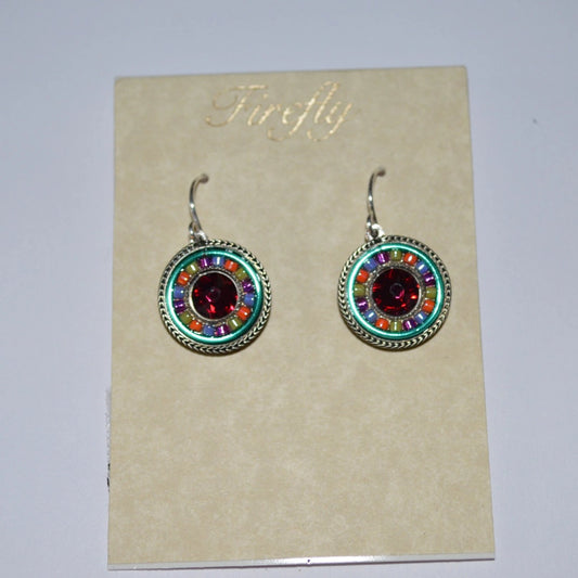 A pair of Firefly Jewelry earrings displayed on a card, featuring multicolored round pendants with intricate embellishments and a central red crystal.