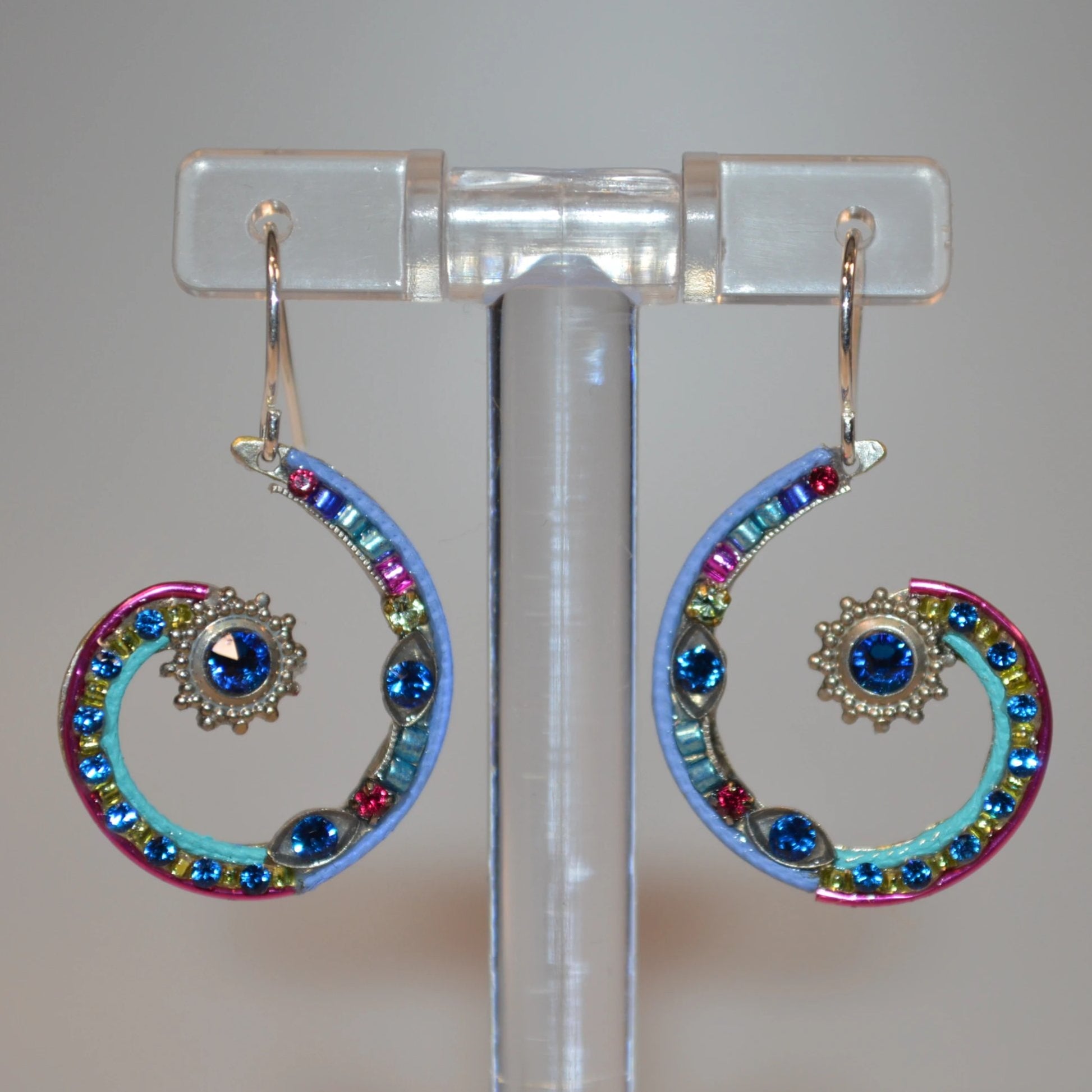 A pair of Firefly Jewelry earrings featuring multicolored embellishments and blue crystals, displayed on a clear stand in close up.