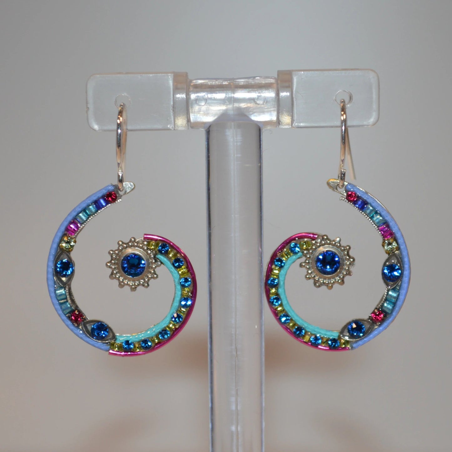 A pair of Firefly Jewelry earrings featuring multicolored embellishments and blue crystals, displayed on a clear stand.