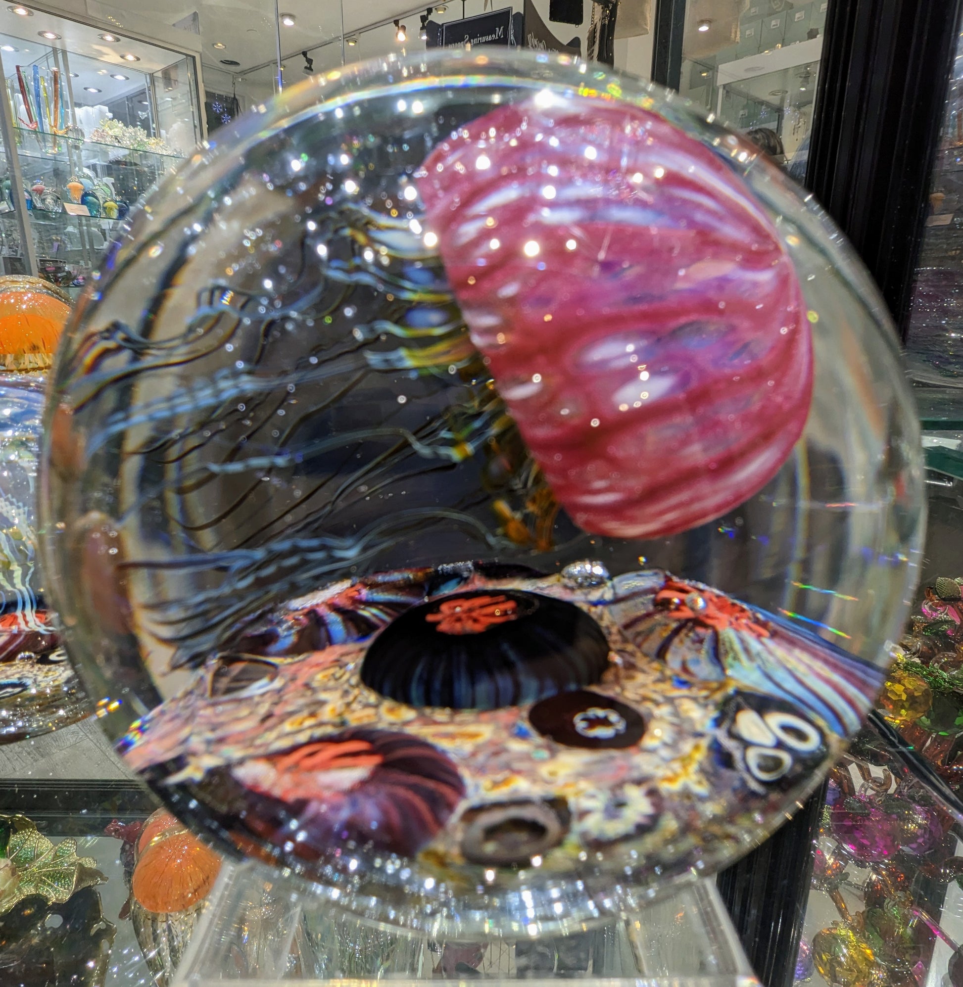 A handcrafted Satava art glass jellyfish sculpture with a gold and ruby colored body, displayed against a clear background