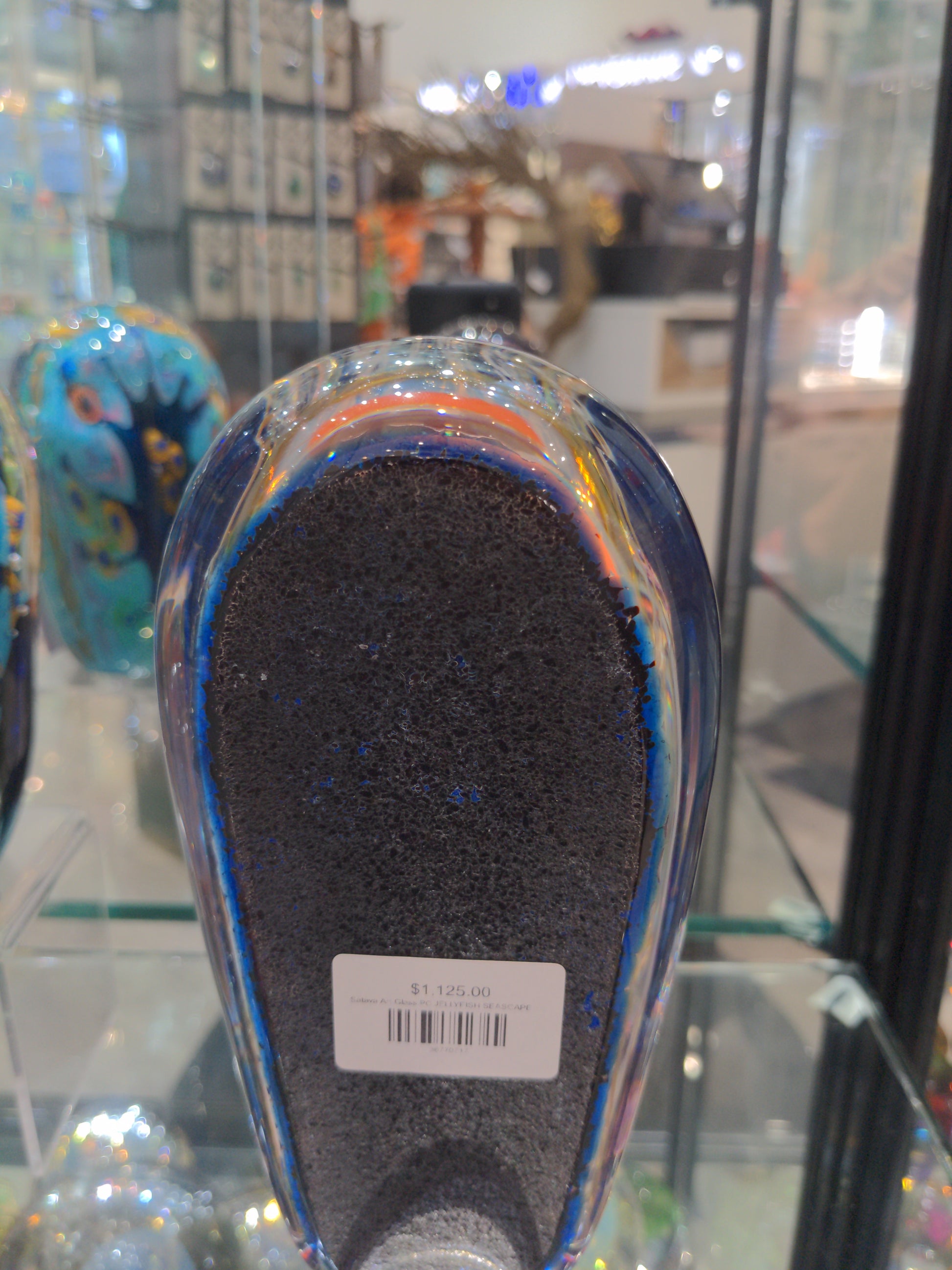 Satava art glass piece featuring an orange jellyfish with a blue background and white tentacles, displayed in a case back view