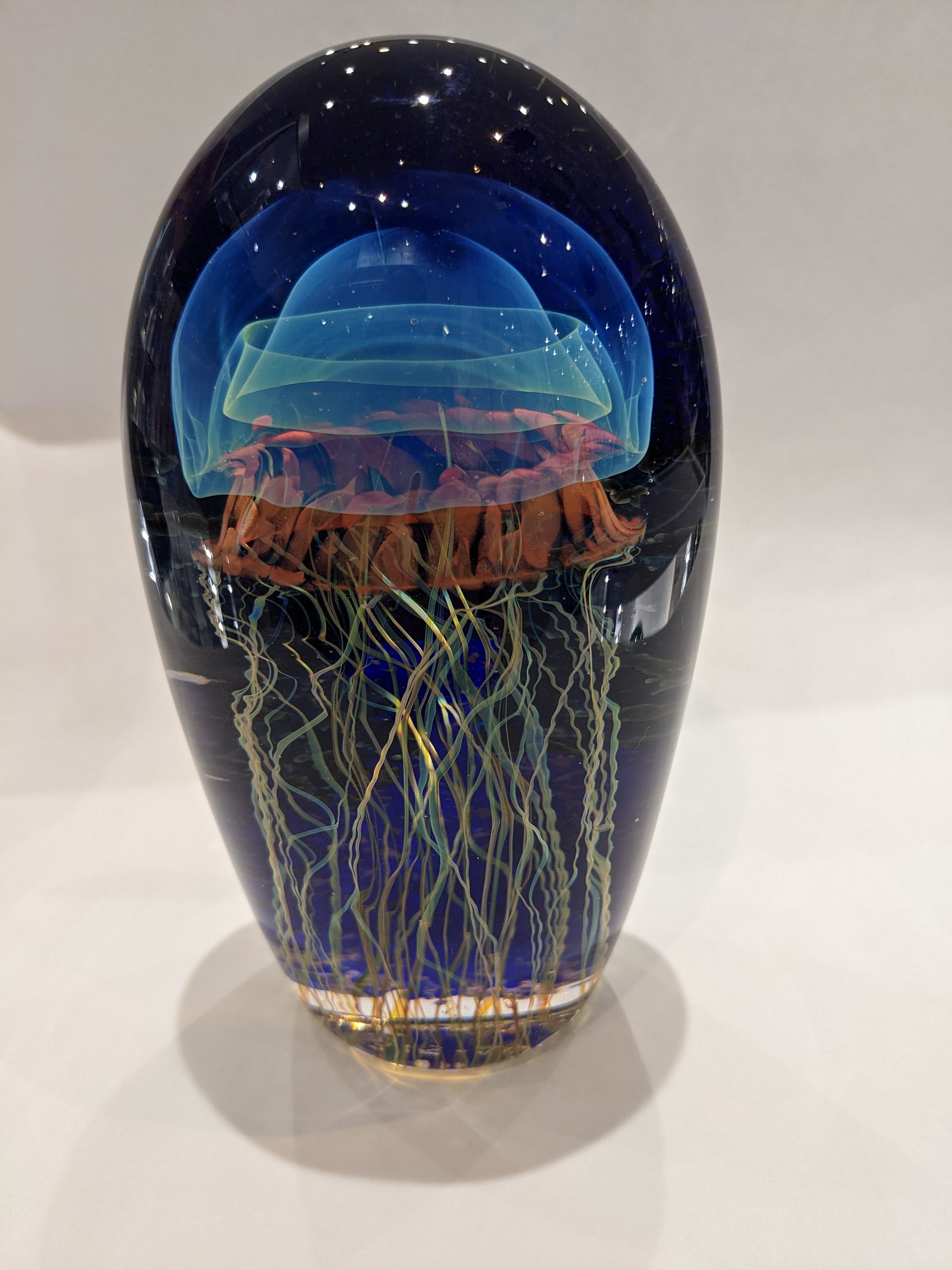 Satava art glass piece with a blue jellyfish design on a moonlit seascape background.