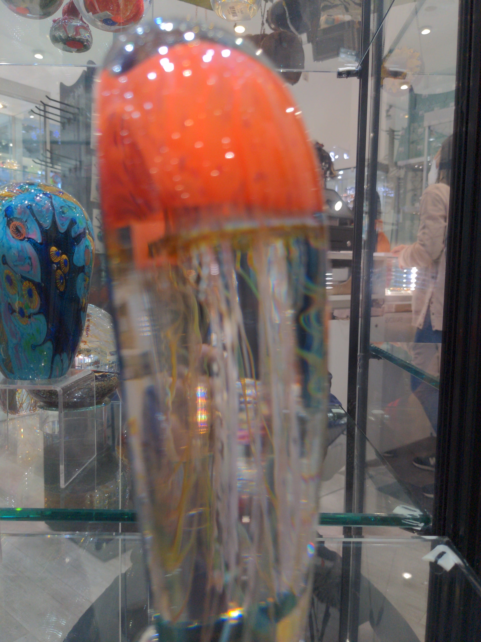 Satava art glass piece featuring an orange jellyfish with a blue background and white tentacles, displayed in a case side view