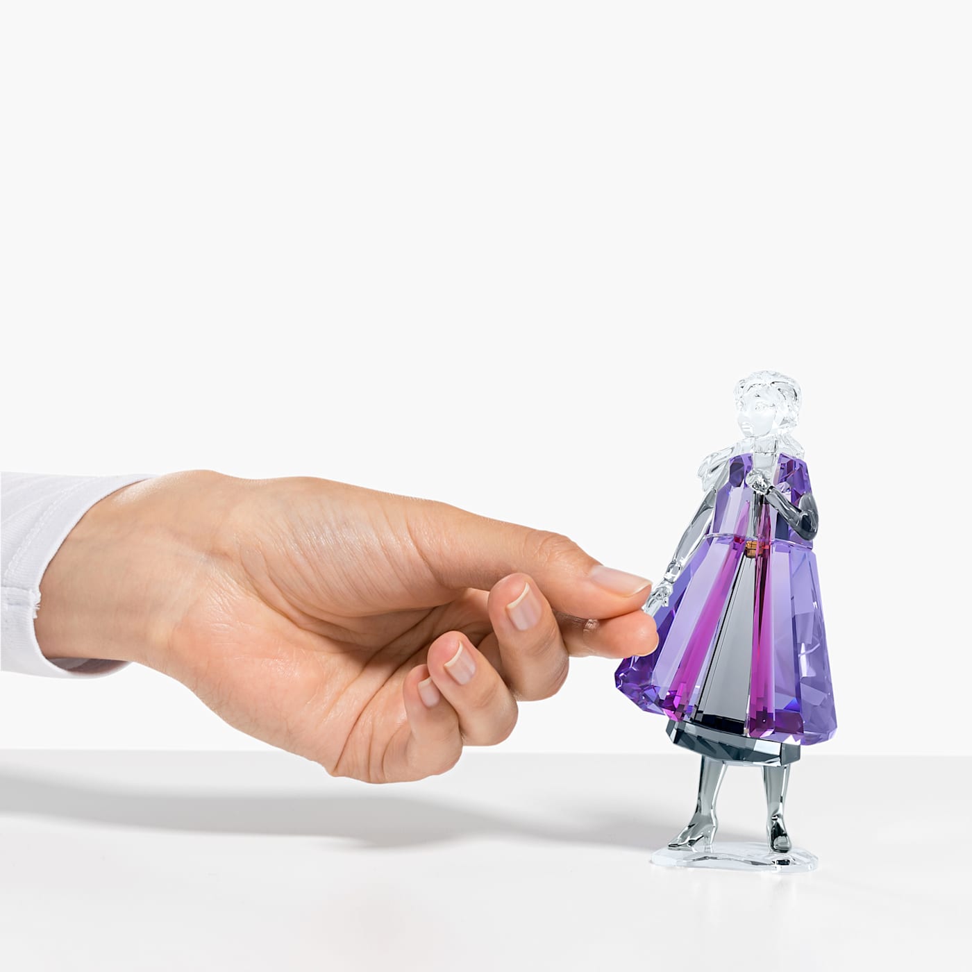 A crystal figurine of Anna from Frozen 2 sits next to a hand.