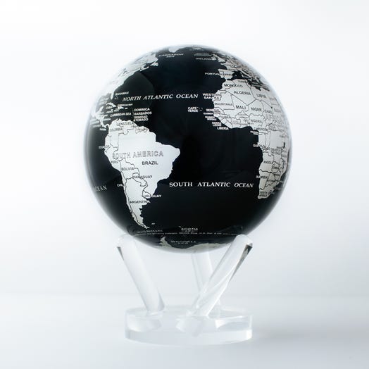 A black and silver MOVA globe with a world map, placed on a clear stand against a white background.