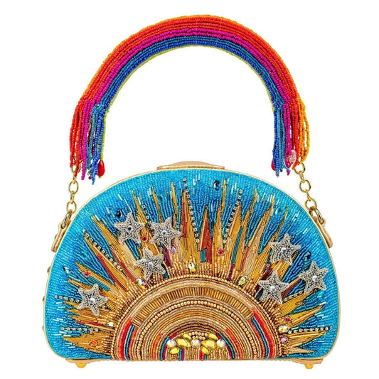 A vibrant blue hand-beaded top handle bag with a golden burst of sunshine design and a rainbow handle with dangling fringe on the ends.
